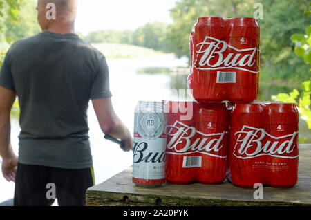 Kharkov, Ukraine - August 10, 2019: Budweiser Bud Bierdosen pack auf alten Tisch und Fischer am Fluss für den Hintergrund. Budweiser ist einer der beliebtesten Stockfoto