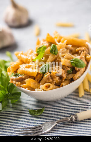 Pasta Penne mit Huhn Stücke Pilze Basilikum und Parmesan italienische Küche in weiße Schüssel am Küchentisch Stockfoto