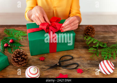 DIY Geschenkverpackung. Frau Verpackung schöne Weihnachten Geschenk auf rustikalen Holztisch. 7/8 Schuß von Weihnachten folierstation. Stockfoto