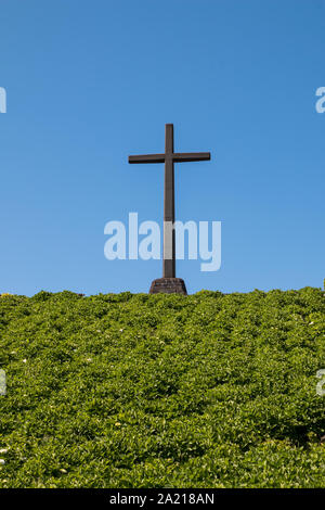 Hermitage (Ermitage de Nossa Senhora da Paz). Großes Kreuz am Horizont. Grüne Pflanzen im Vordergrund. Strahlend blauen Himmel. Vila Franca do Campo, Sao Mig Stockfoto