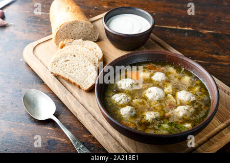 Hausgemachte Suppe mit Fleischbällchen in einem Ton Teller auf dem Tisch. Platte steht auf einem sackleinen Serviette. Hot home Abendessen Stockfoto