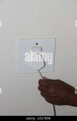 Nahaufnahme einer Hand, die Kabel vom Stecker eines Gerätes auf weißem einzelne Steckdose. Stockfoto
