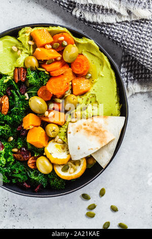 Avocado Hummus mit gebackenem Gemüse, Oliven, Nüsse und Beeren in eine schwarze Platte. Gesunde vegane Ernährung Konzept. Stockfoto