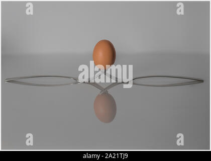 'S Chicken Egg auf zwei Gabeln ausgeglichen, mit einer Reflexion. Stockfoto