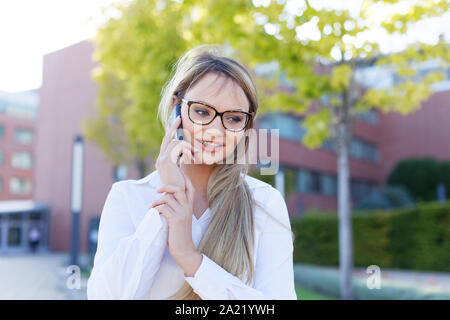 Gerne blonde junge geschäftsfrau in Brillen Aufruf im Park, auf der Suche Stockfoto