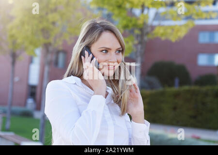 Gerne blonde junge geschäftsfrau Aufruf im Park, auf der Suche Stockfoto