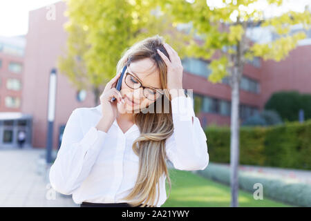 Blonde junge geschäftsfrau Kopfschmerzen während der Aufruf in Park Stockfoto