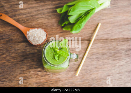 Mason Glas Tassen mit grünem Spinat, Bananen und Kokosmilch Gesundheit Smoothie mit einem Löffel Haferflocken auf Holz rustikalen Tisch gefüllt Stockfoto