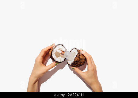 Ansicht von oben weibliche Hände, die Flasche kosmetische Öl zwischen zwei Hälften eines frisch gerissenen Coconut auf weißem Hintergrund, flach. Stockfoto