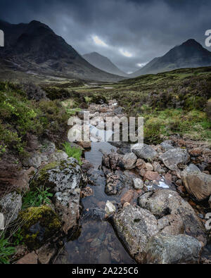 Dramatische Himmel mit dunklen Wolken über dem malerischen, grünen Tal mit Stream und Felsen. Glencoe in den schottischen Highlands. Landschaft Bild mit Atmosphäre. Stockfoto