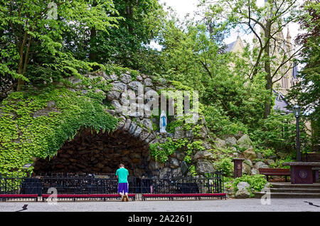 Grotte Unserer Lieben Frau von Lourdes; junger Mann, beten, knien, beleuchtete Votiv Kerzen; religiöse Heiligtum; Stein, Efeu, Katholisch; Universität von Notre Dame; Stockfoto