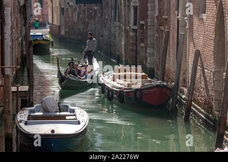 Die Leute, die ein traditionelles Gondelfahrt in einem schmalen Kanal in der Sonne Venedig Italien Stockfoto