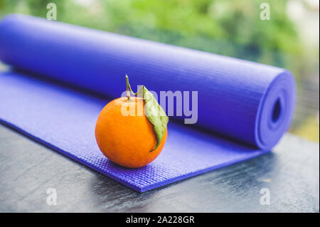 Yoga Matte, Wasser, orange und Mango auf einer hölzernen Hintergrund. Ausrüstung für Yoga. Konzept gesunde Lebensweise, Ernährung und Sport. Kopieren Sie Platz. Selektiver Fokus Stockfoto