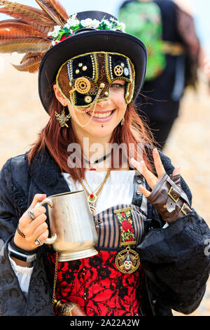 Piraten Tag, Hastings. Schönen Kaukasischen junge Frau mit verzierten Gesichtsmaske über einem Auge. Auf Viewer und lächelnd, während sie Bier Tankard. Stockfoto