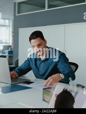 Eine junge männliche Unternehmer mit Laptop arbeiten auf Berichte im Büro Schreibtisch sitzen Stockfoto