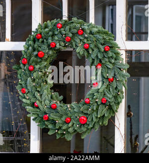 Streen Weihnachtsdekoration, große runde Weihnachten Kranz aus natürlichen Tanne mit roten Äpfeln hängen an Fenster schließen eingerichtet, Stockfoto