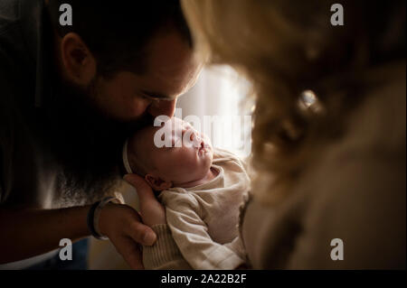 Vater küssen Schlafen neugeborene Töchter Kopf im Arm der Mutter