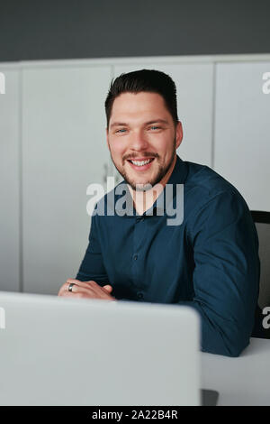 Porträt einer gut gekleidete junge Unternehmer lächelnd souverän sitzt mit Laptop Kamera schaut im Büro Schreibtisch Stockfoto