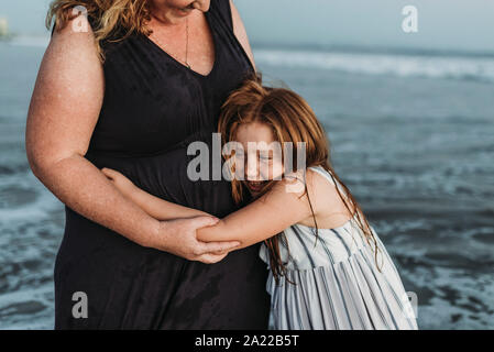 Seitenansicht der glückliche junge Tochter umarmen Mutter im Ozean bei Dämmerung Stockfoto