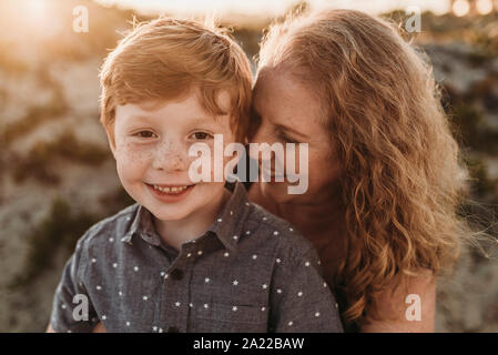 Vorderansicht von Mutter umarmt redheaded Kindergarten alter Sohn bei Sonnenuntergang Stockfoto