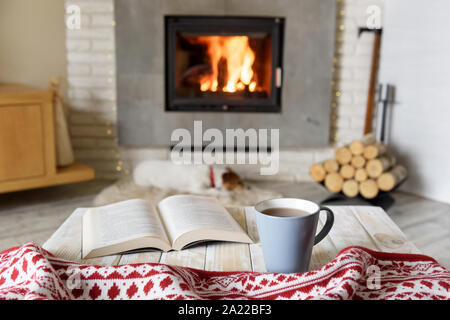 Hygge Konzept mit offenem Buch und einer Tasse Tee in der Nähe von brennenden Kamin
