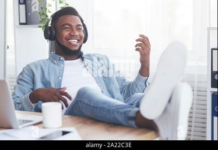 Bei der Arbeit. Fröhlich afrikanische amerikanische Mitarbeiter Musik hören über Kopfhörer und spielen virtuelle Gitarre, Entspannung am Arbeitsplatz Stockfoto