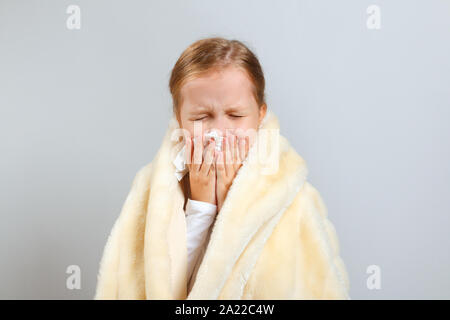 Kleines Mädchen bläst die Nase, in einem Plaid gewickelt, auf grauem Hintergrund. Stockfoto