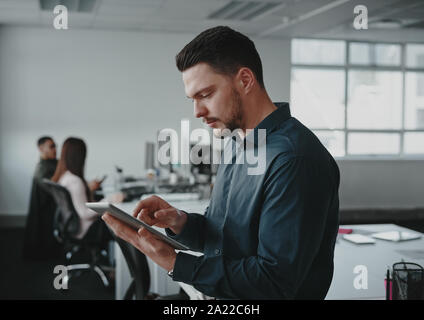 Portrait der junge Unternehmer besetzt mit digitalen tablet, während sein Kollege im Hintergrund bei modernen Büro arbeiten Stockfoto