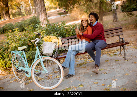 Multiratial junge Liebende Paar sitzt auf der Bank im Herbst City Park Stockfoto