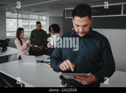 Young Professional Geschäftsmann mit digitalen Tablet während seine Kollegen in die Diskussion über Projekt im Hintergrund Stockfoto