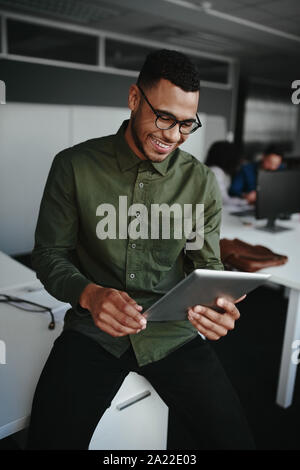 Lächelnde junge Unternehmer online arbeiten auf digitalen Tablet beim Sitzen am Schreibtisch in einem Büro Stockfoto