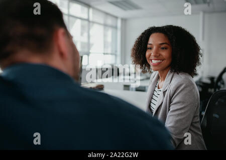 Junge lächelnde schöne Geschäftsfrau im Gespräch mit einem männlichen Kollegen am Arbeitsplatz Stockfoto