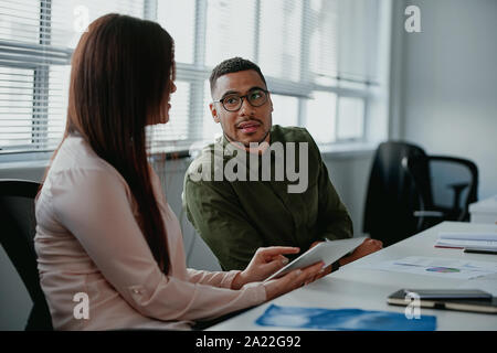 Junge Geschäftsfrau über etwas Positives mit digitalen Tablet mit ihren männlichen Kollegen am Arbeitsplatz Stockfoto