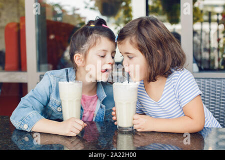 Zwei lustige Kaukasischen wenig Vorschule Geschwister Geschwister trinken Milchshakes im Cafe. Freunde Mädchen Spaß zusammen haben. Kalten Sommer Desserts für Kinder. Hap Stockfoto