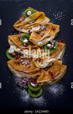 Dünne Crepes mit geschmolzener Schokolade, Sesam, Granatapfel und Mandeln Stockfoto
