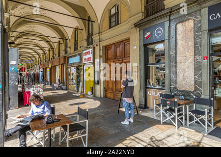 Ein Mann liest eine Zeitung und trinkt Kaffee an einem Tisch in der Bar Sacchi in einem Portikus entlang der Via Sacchi, Turin, Italien Stockfoto