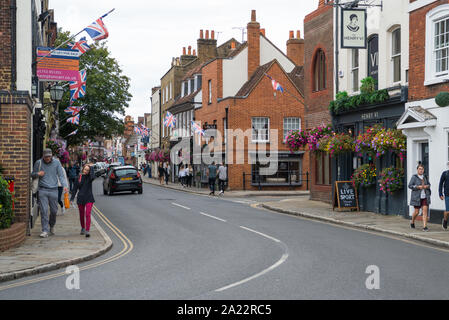 Die Menschen in der High Street, Eton. Bunte Szene mit Blumen bepflanzten Ampeln und Union Jack Fahnen. Stockfoto