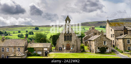 Panorama von grünem Weideland für Schafe mit Trockenmauern hinter Gemeindekirche und Steinhütten in Reeth North Yorkshire England Stockfoto