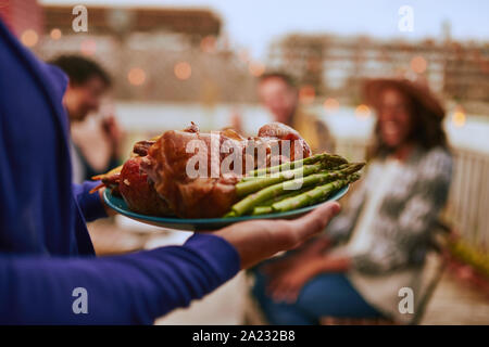 Tausendjährigen Freunde essen Truthahn Abendessen mit Spargel auf einer Platte draußen serviert auf einer Dachterrasse für Thanksgiving und Sonnenuntergang Stockfoto