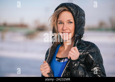 Porträt eines sportlichen blonde Frau fit halten einen kalten Wintertag durch Spazieren gehen, in eine verschneite Stadt Stockfoto