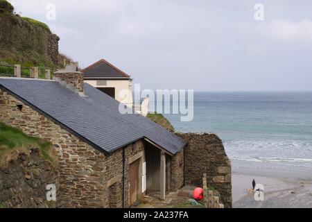 Trevaunance Cove, die hl. Agnes, North Cornwall, UK. Seascape steinerne Gebäude auf Trevaunance Punkt mit einem Hund Walker am Strand an einem Frühlingsmorgen. Stockfoto