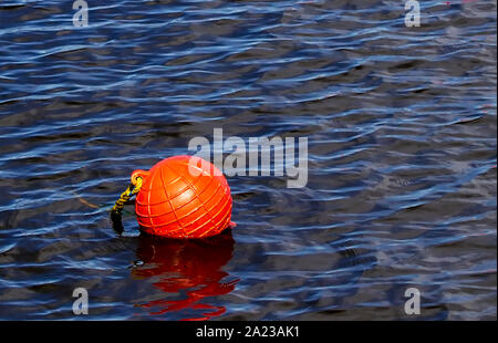 Ein helles orange Boje schwimmt auf der Wasseroberfläche. Nahaufnahme des Bereichs Sicherheit Bojen in einem See mit kleinen Wellen auf der Wasseroberfläche. Stockfoto