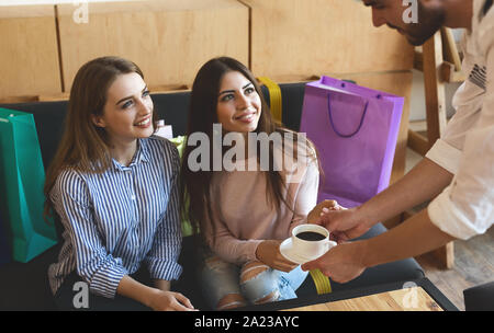 Freundlich zu sein. Kellner Kaffee für zwei fröhliche Mädchen im Cafe bringen Nach dem Einkaufen Stockfoto