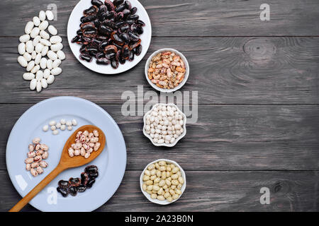 Sammlung von Bohnen und Hülsenfrüchte auf Holzlöffel und auf die Platten über Holz- Hintergrund. Eine Reihe von verschiedenen Bohnen. Wohnung mit Kopie Raum legen. Stockfoto