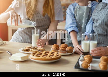 Gesundes Mittagessen. Frau gießen Milch in Gläser, Familie in Snack an Küche, 7/8 Stockfoto