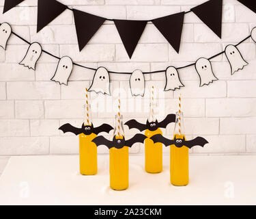 Halloween Party. Flaschen mit gelben Cocktail und Papier Fledermäuse auf der Oberseite über weiße Steine Wand Stockfoto