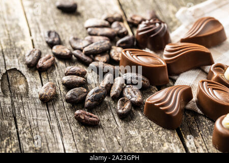 Verschiedene Pralinen und Kakaobohnen auf alten Holztisch. Stockfoto