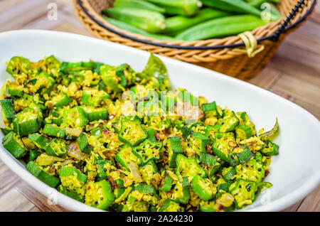 Nahaufnahme von Okra Pfannengerichte mit Kokosraspeln in eine ovale Schale mit Finger frische Dame in einem Korb im Hintergrund Stockfoto