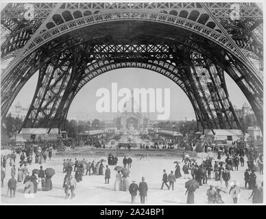 Paris Exposition, Blick vom Boden auf den Eiffelturm mit Pariser Promenierenden; Foto zeigt einen Blick auf die Basis der Eiffelturm in Richtung der zentralen Kuppel des Palais des Industries an der Exposition Universelle de 1889, in Paris, mit Fußgängern zu Fuß im Vordergrund.. Stockfoto