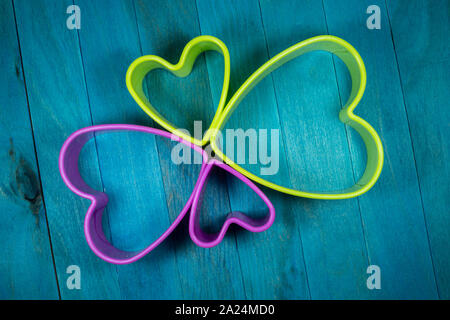 Farbige herzförmige Ausstechform Zahlen bilden eine dekorative Blüte, sitzen auf den blauen Hintergrund und Holz gesehen von oben Stockfoto